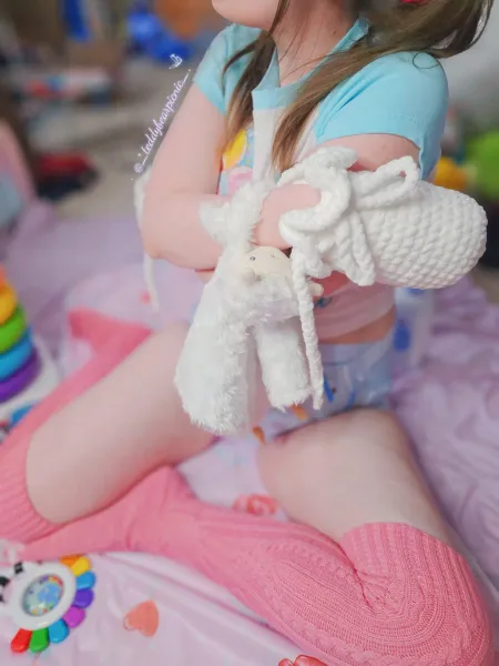 An ABDL girl wearing pink knee-high socks and showing off her diaper.