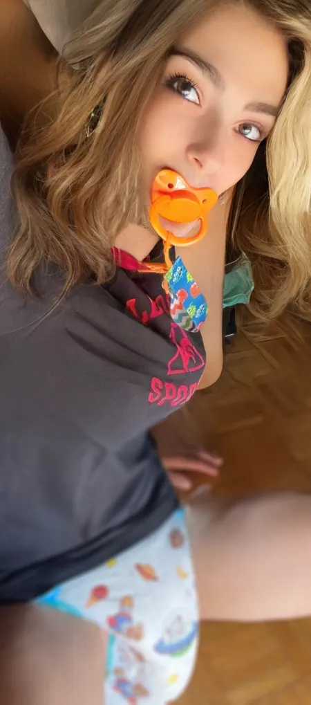 Young woman in black sporty top sucking pacifier, white printed diaper hugging her curvy hips and thick thighs