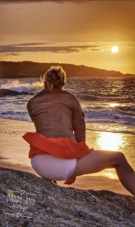 A girl squatting on the sunset beach in a white diaper, her plump, juicy buttocks.