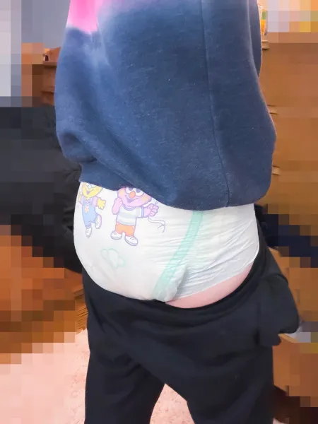 A girl pulling down her black pants to show off her diapered bottom.