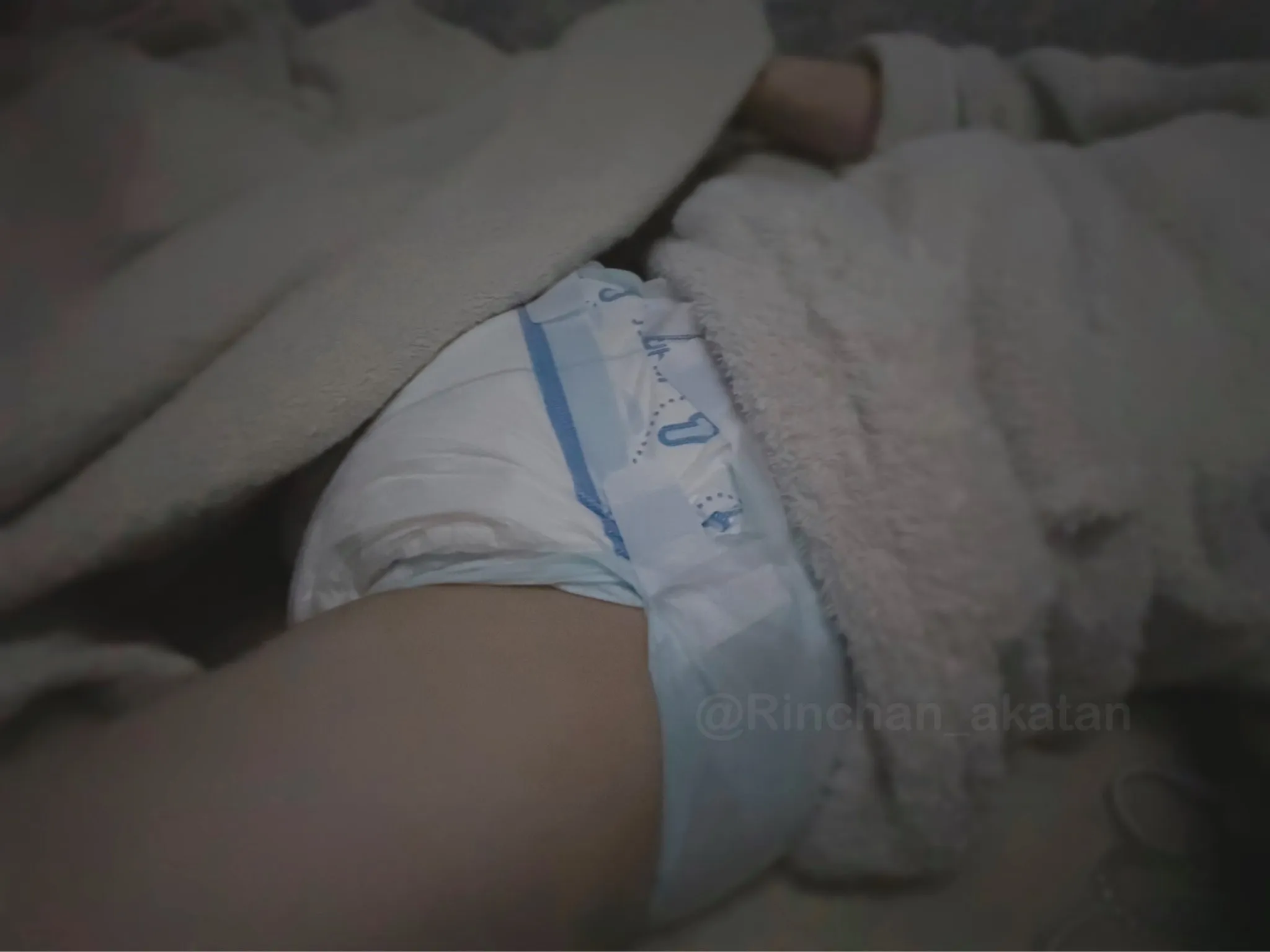 An ABDL girl lies wearing woolen clothes, with a diaper fastened on her lower body.