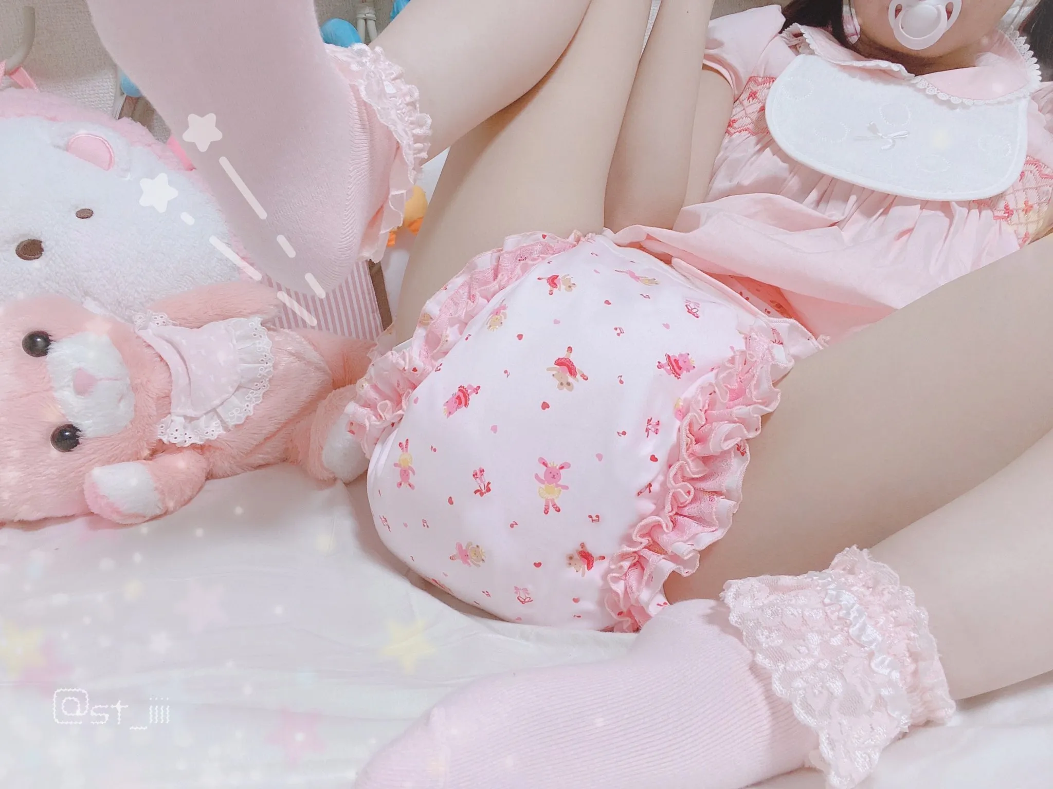 An ABDL girl is lying in bed wearing a pink diaper cover and assuming a diaper-changing position.