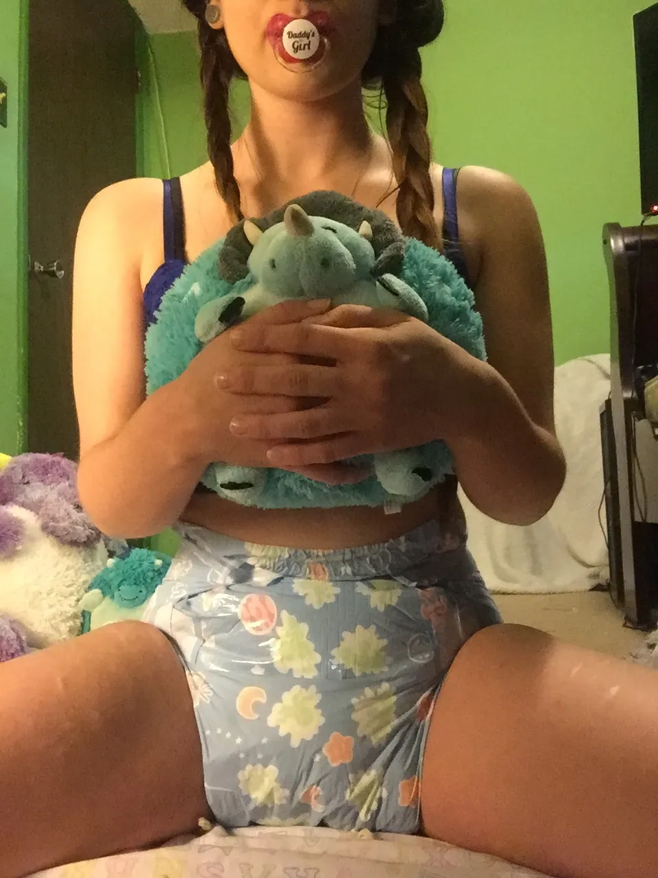 An ABDL woman is wearing a blue lace camisole and blue ABDL diapers while sucking on a pacifier.