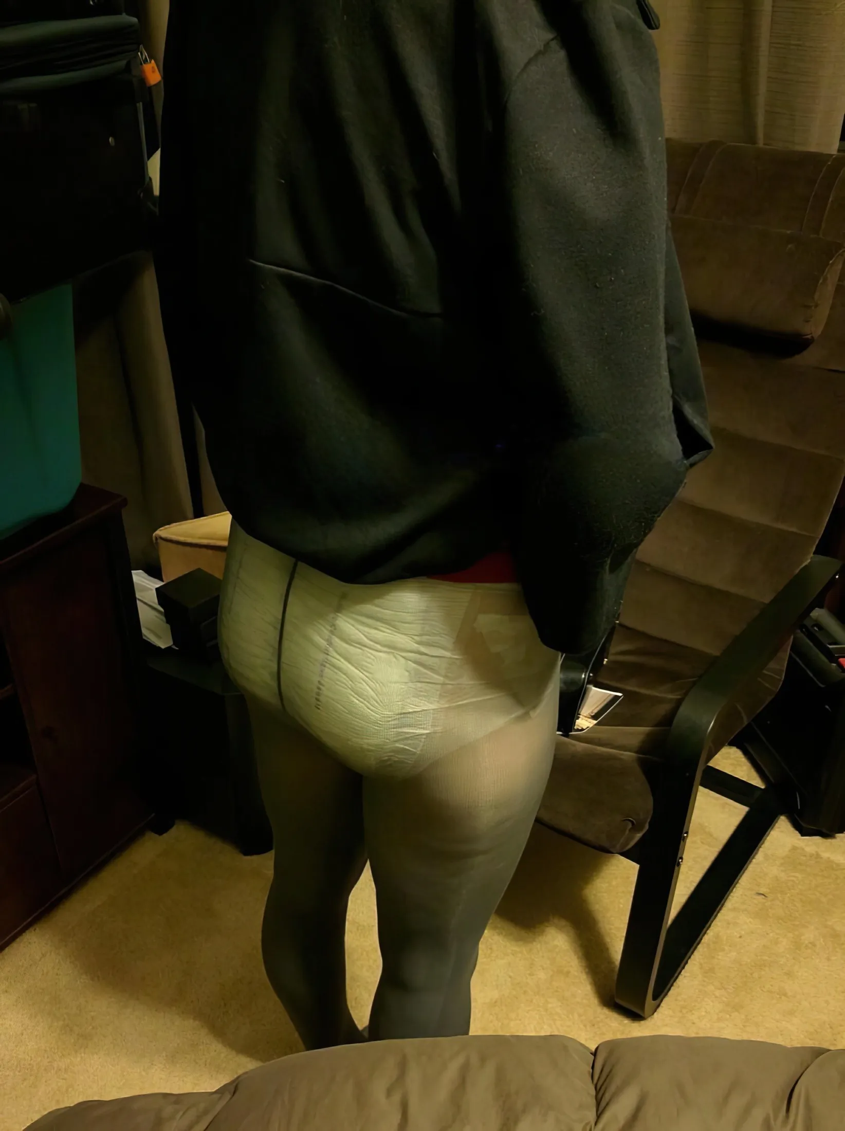 An ABDL woman stands wearing a diaper inside black stockings.