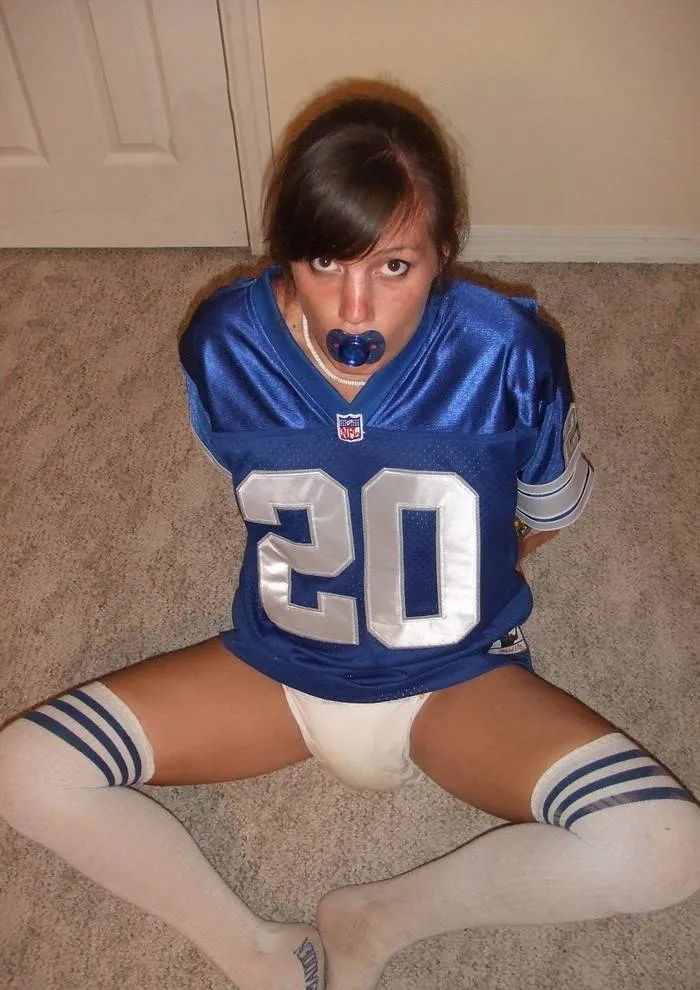 An ABDL girl is exposed in a wet diaper while bound in football attire.