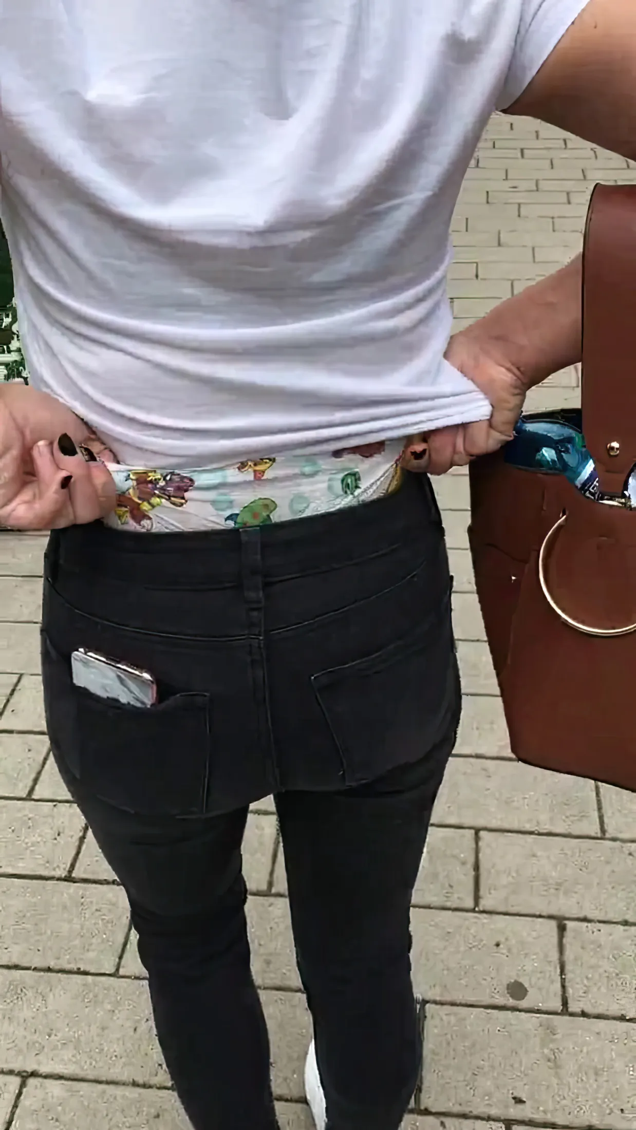 An ABDL girl is pulling a diaper over her denim pants outdoors.