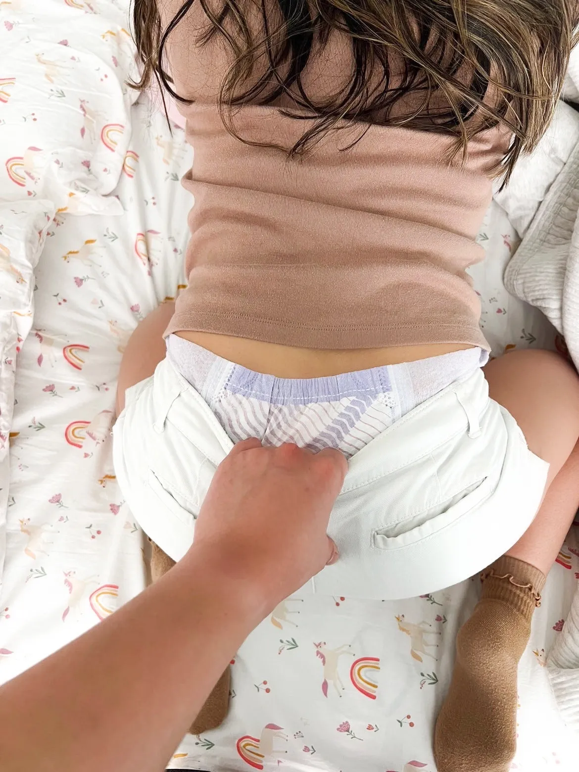 An ABDL girl had her shorts pulled down by a man's hand, exposing her diaper.