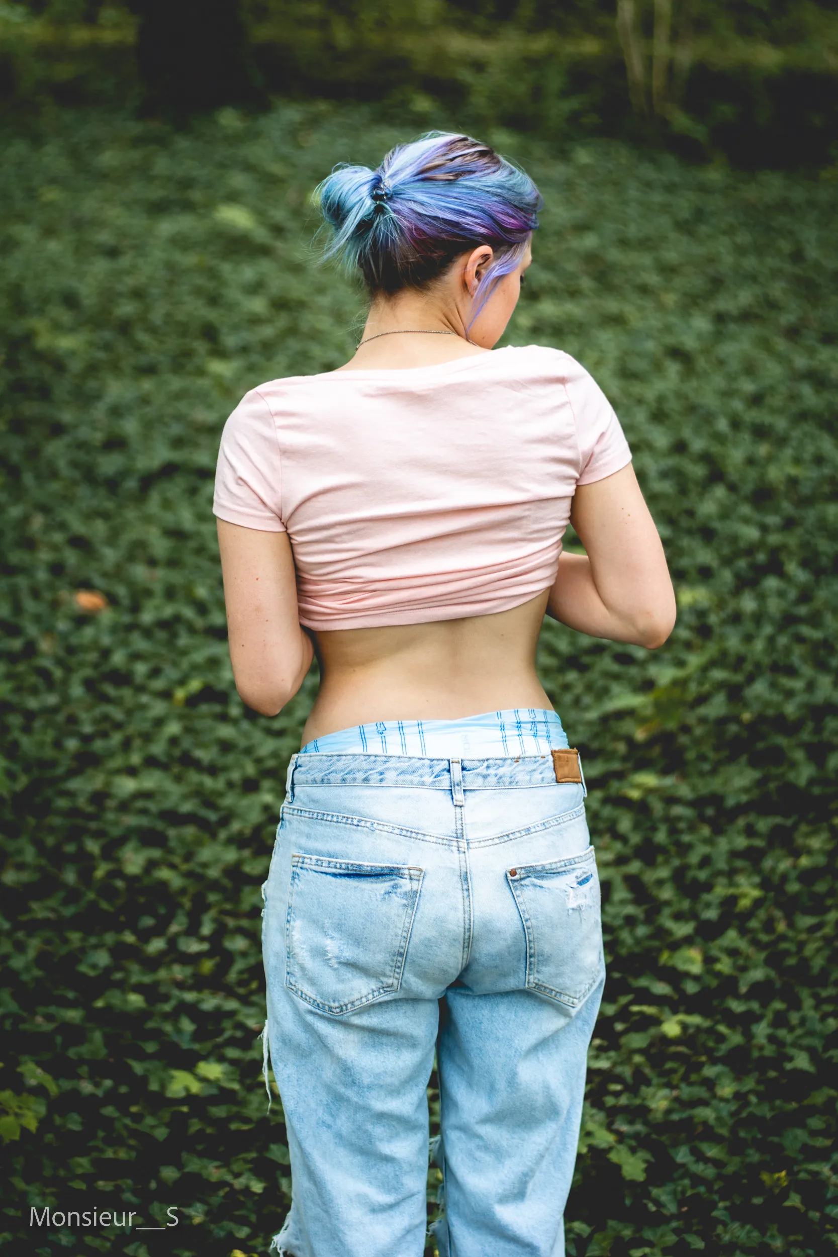 An ABDL girl shows off her diaper and jeans from behind outdoors.