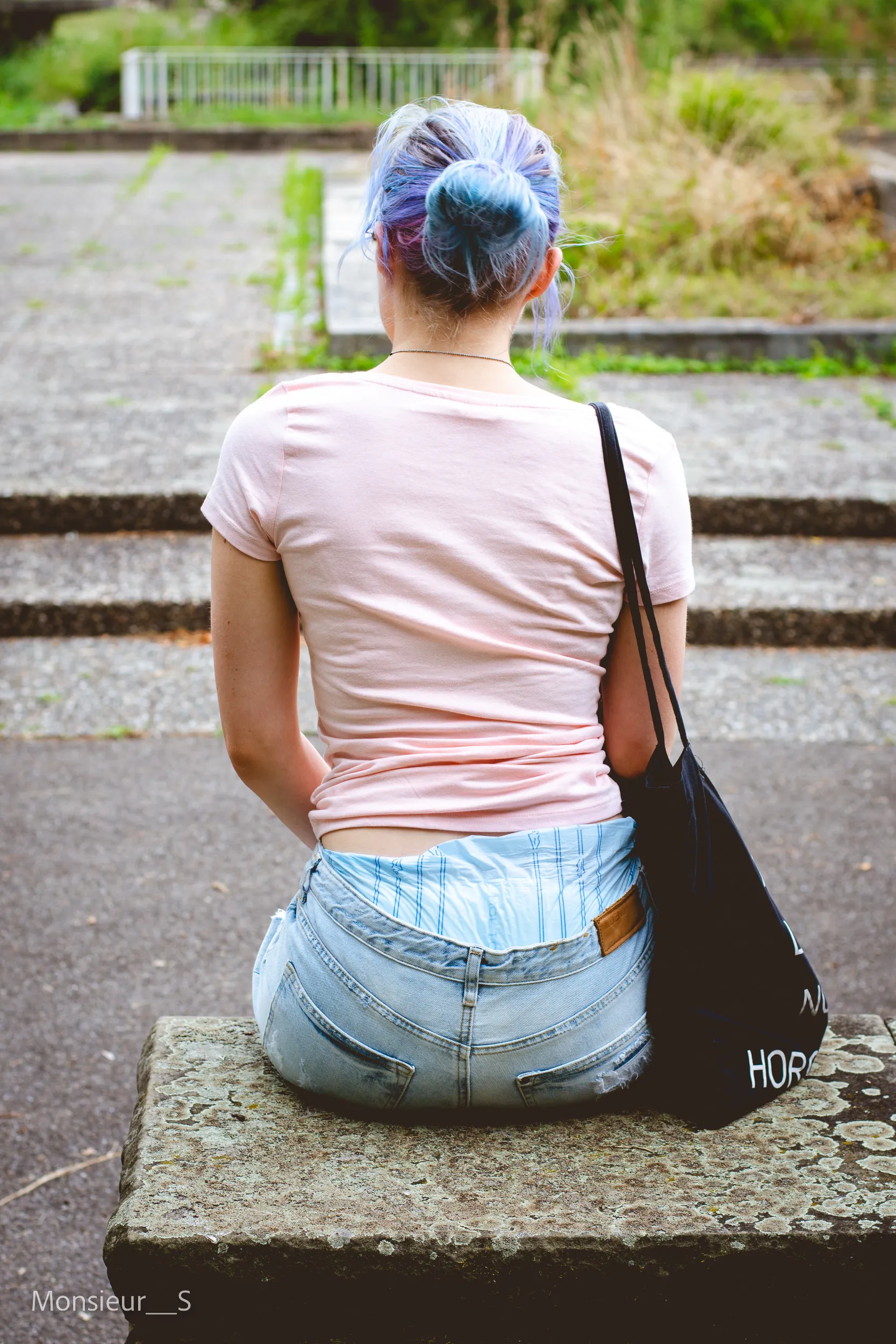 An ABDL girl shows off her diaper and jeans from behind outdoors.