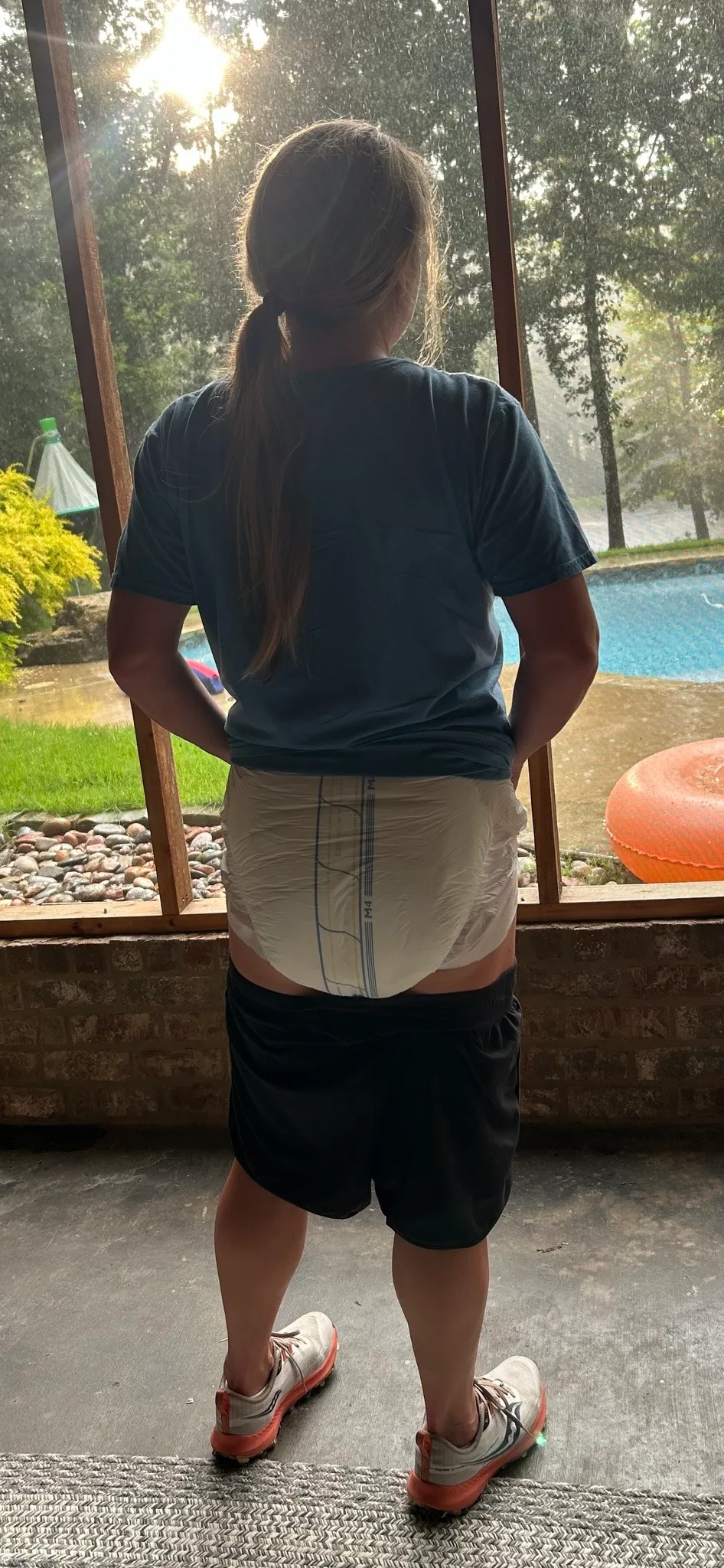 An ABDL woman pulls down her shorts outdoors to show off her diaper.