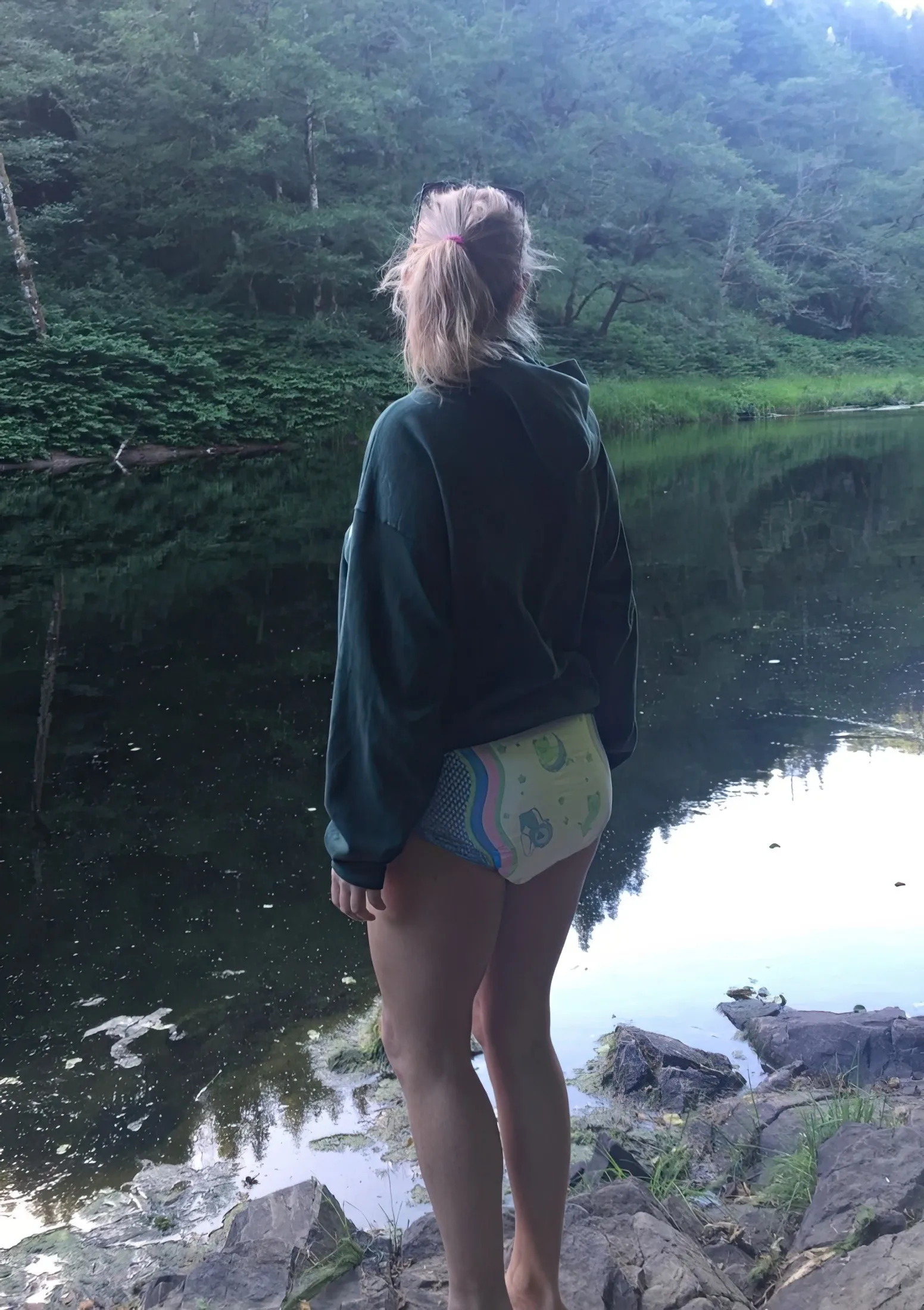 An ABDL girl stands by the riverbank, exposing her diaper.
