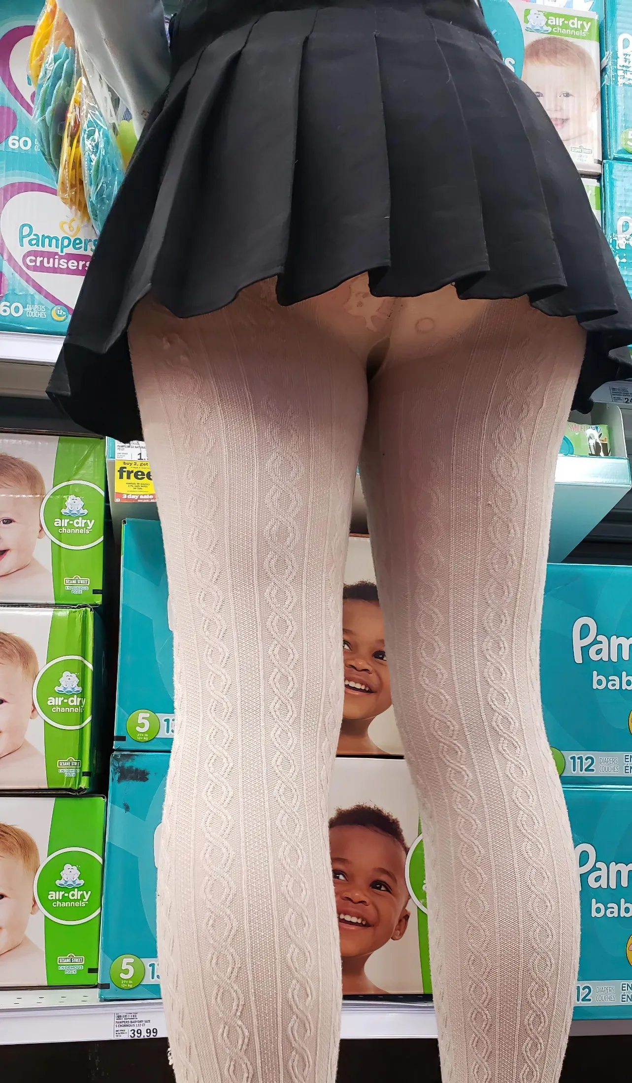 An ABDL girl stands in front of the diaper display wearing white stockings and a diaper.