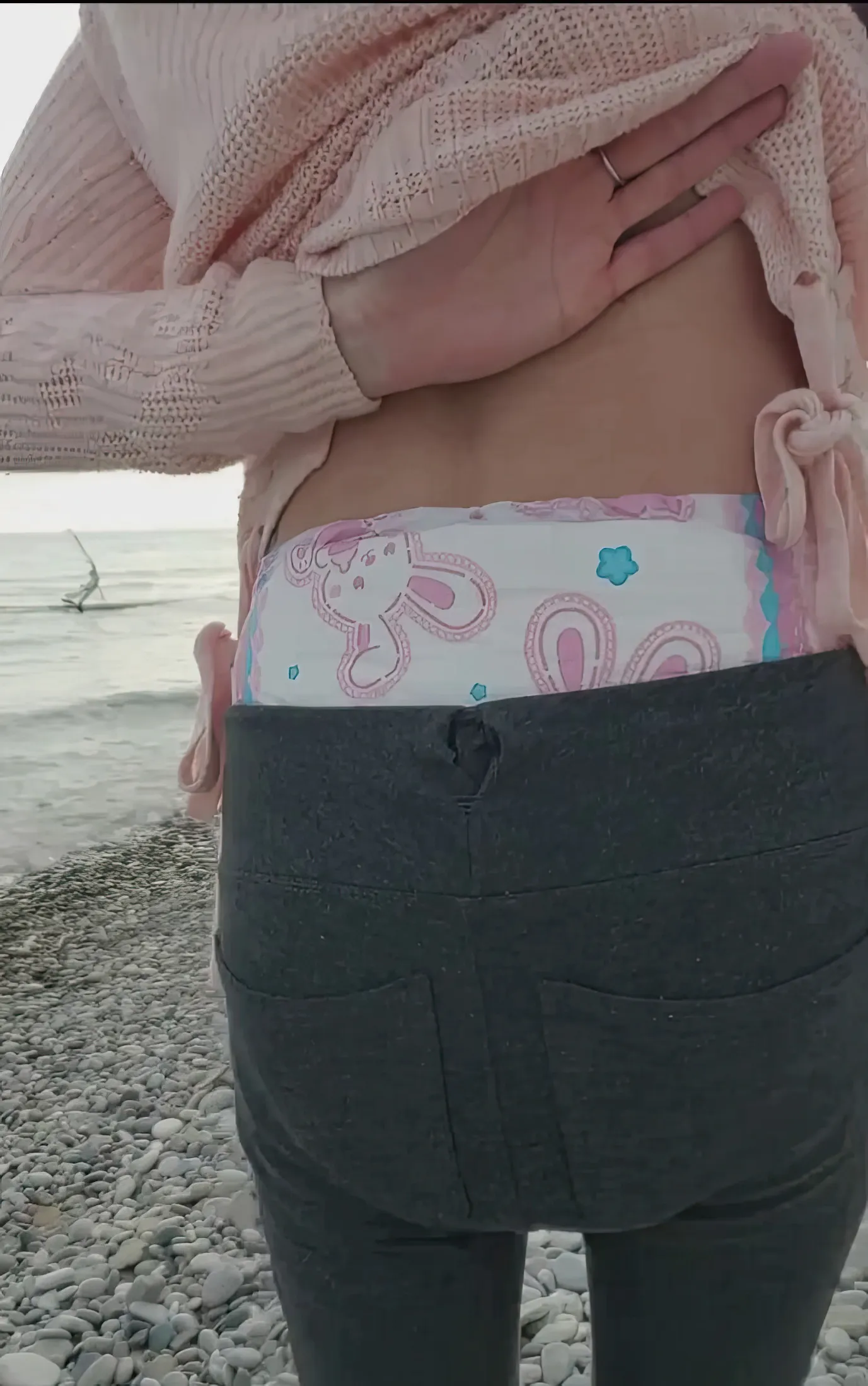 When the ABDL girl lifts her top at the beach, the waistband of her Bunny Hops diaper is visible. Her butt is also incredibly plump.