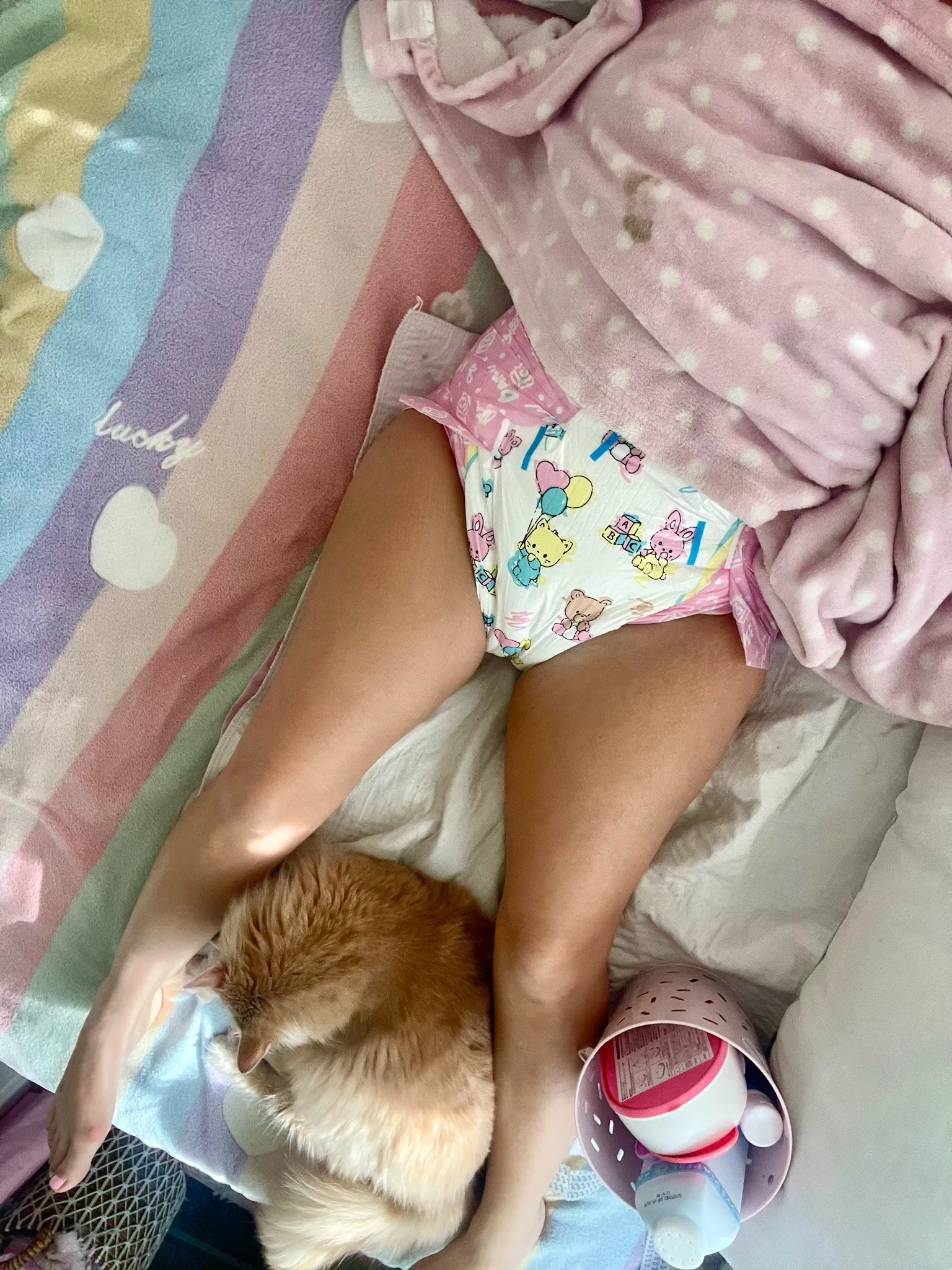 An ABDL girl lies in bed wearing a diaper alongside a cat.