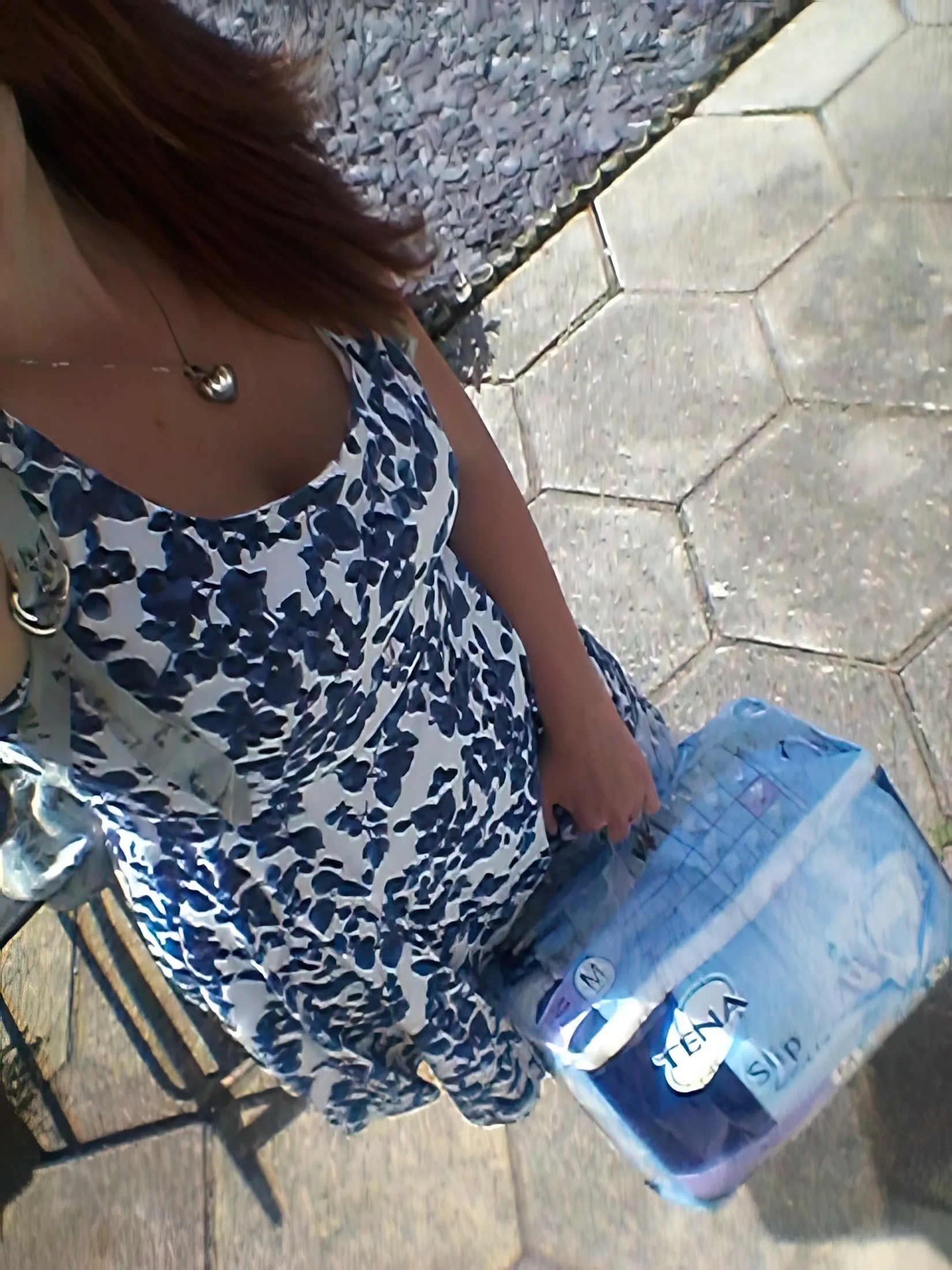An ABDL woman stands outdoors holding a Tena Slip diaper.