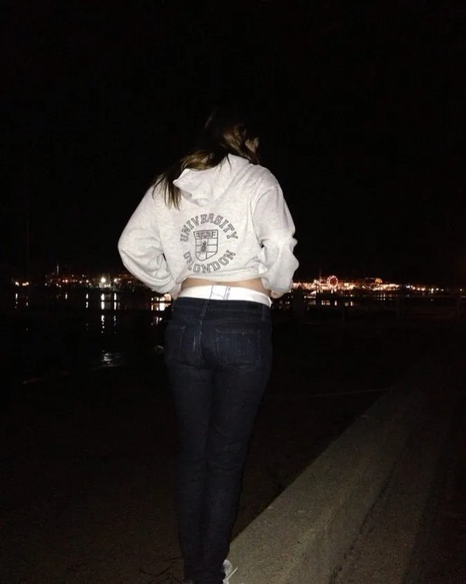 An ABDL girl exposes her diaper band over her jeans outdoors.