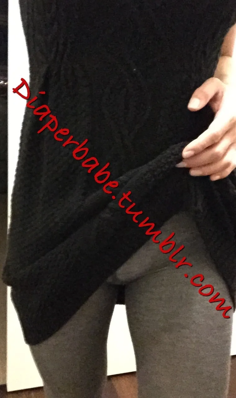 As the ABDL woman lifts her black top, the diaper is visible beneath her gray leggings.