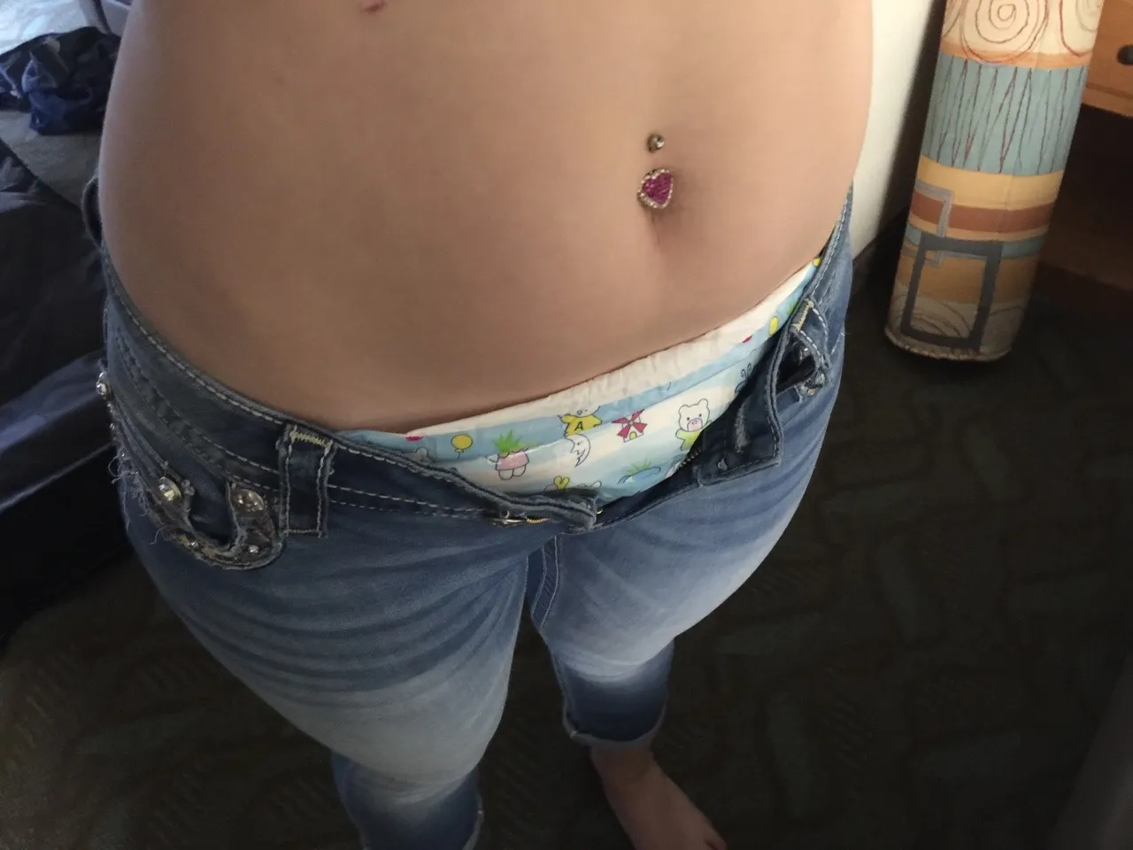 The ABDL girl's jeans are unbuttoned, revealing her diaper peeking through.
