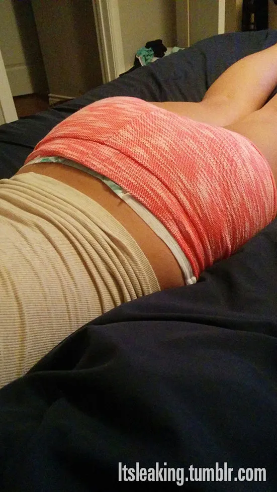 ABDL girl is lying face down wearing diapers under red shorts.