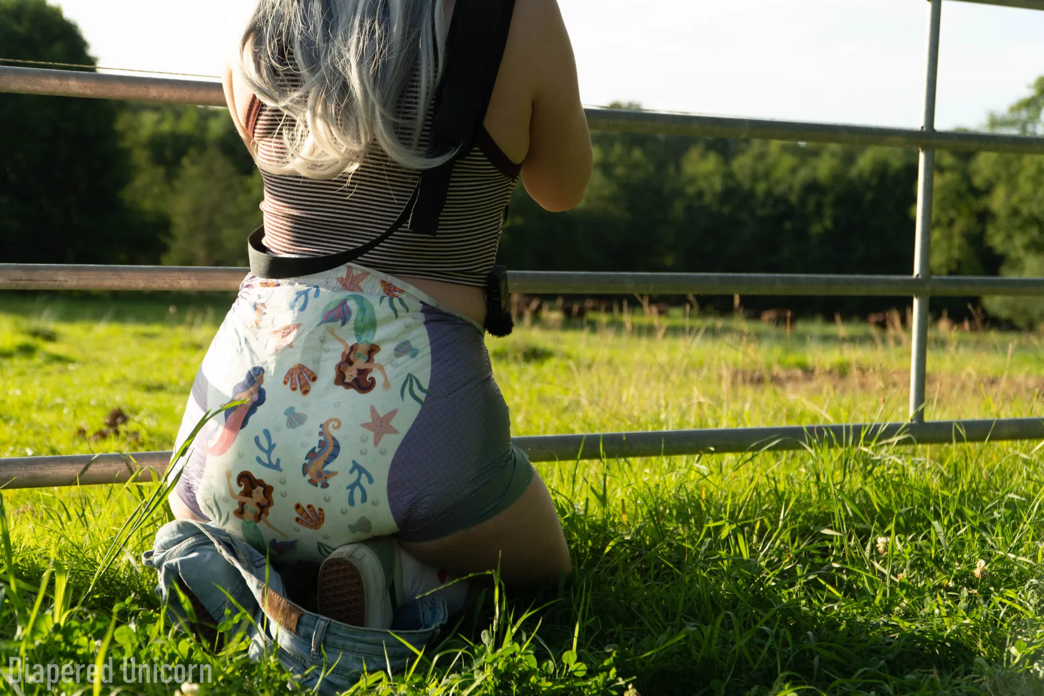 An ABDL girl is showing off in the grass wearing only a diaper underneath.