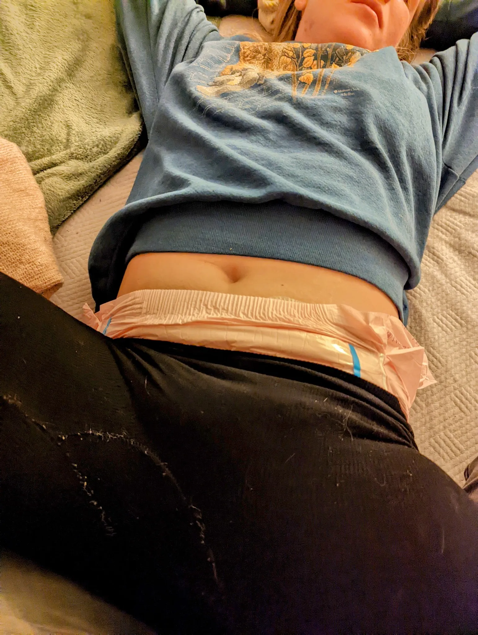 An ABDL girl is sitting on a motorcycle outdoors wearing a string tank top and diapers.