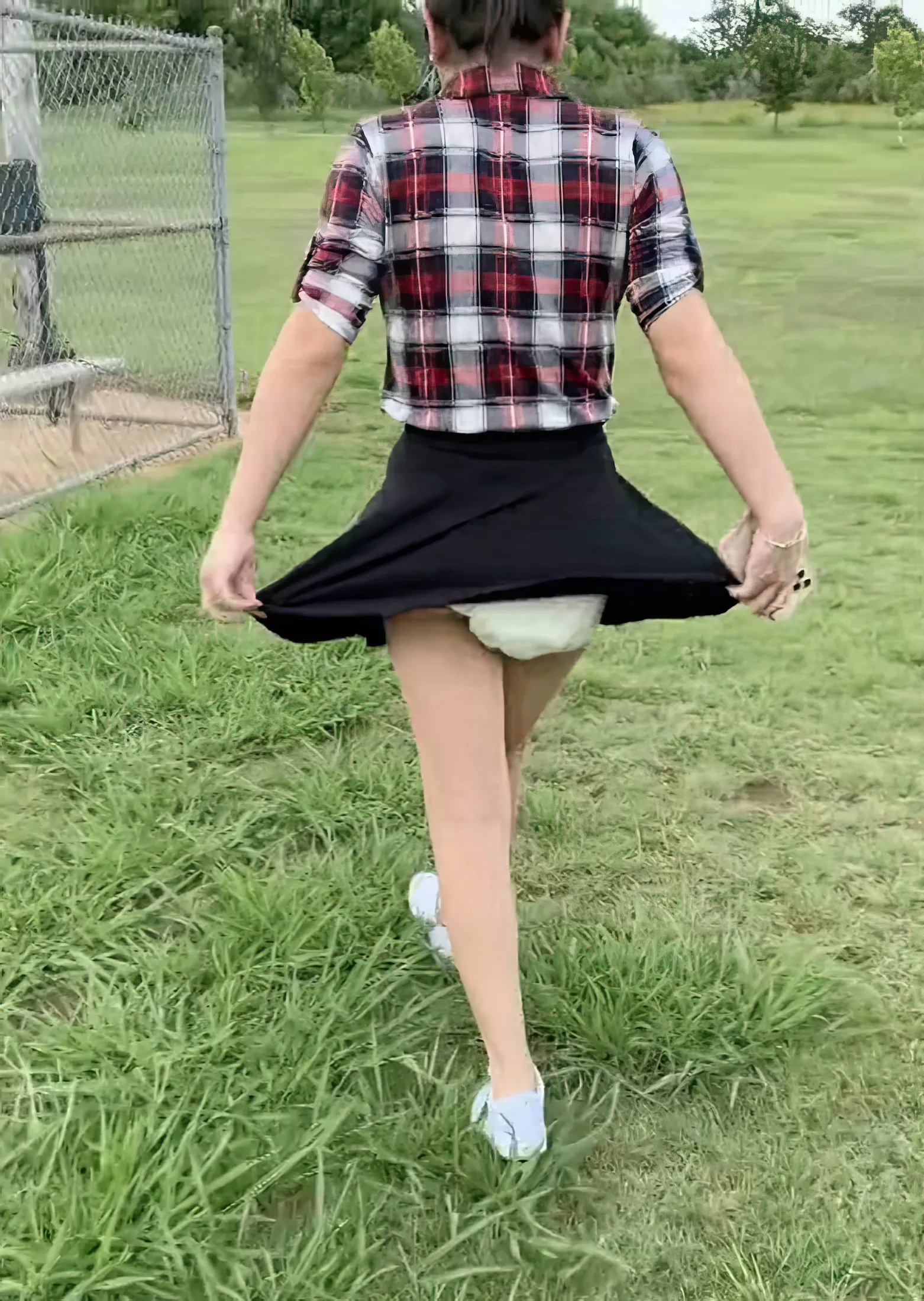 An ABDL girl pulls her skirt aside in a field to expose her diaper.
