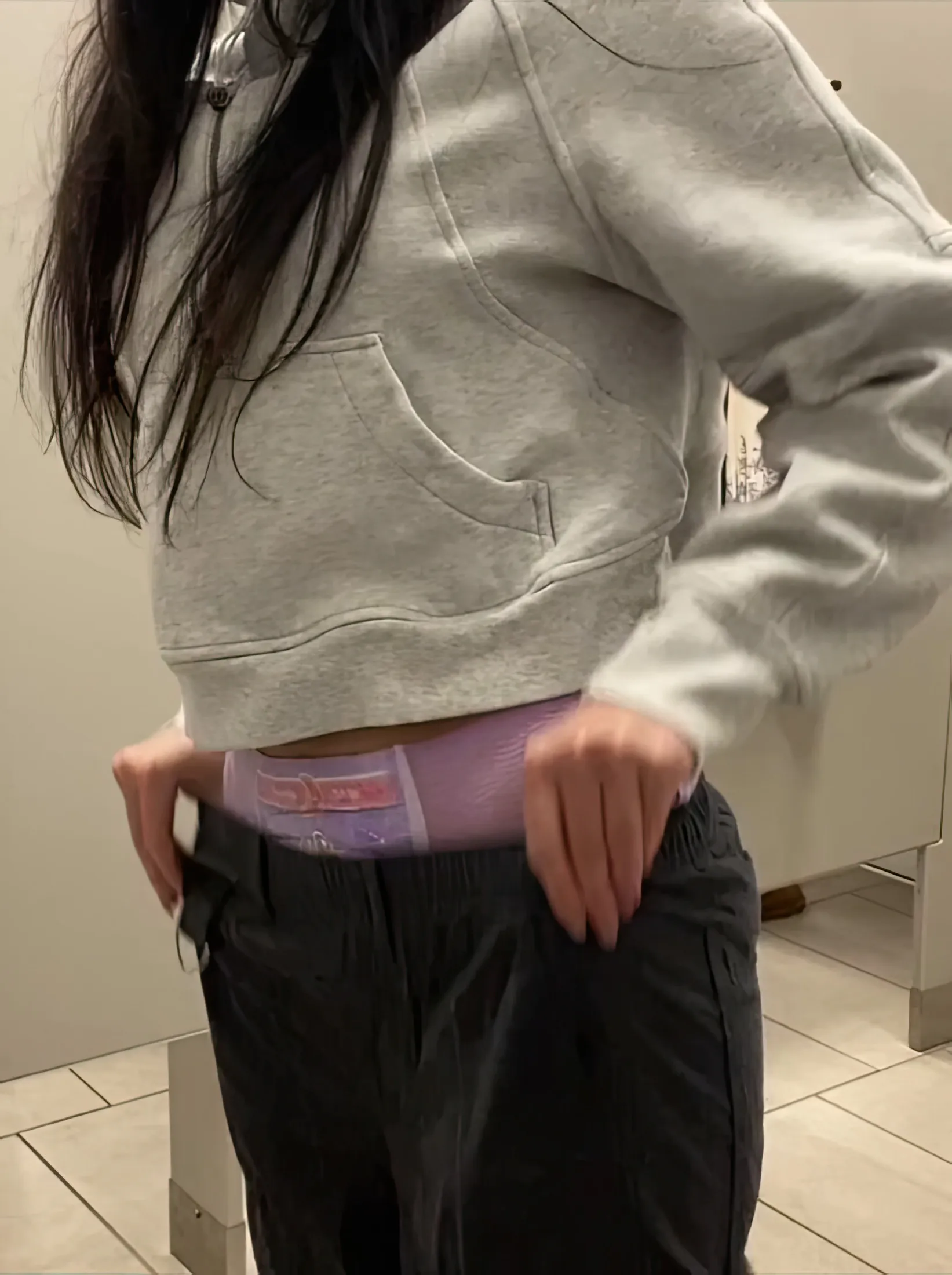 The ABDL girl pulls up her pants. The waistband of the pull-up diaper is visible.
