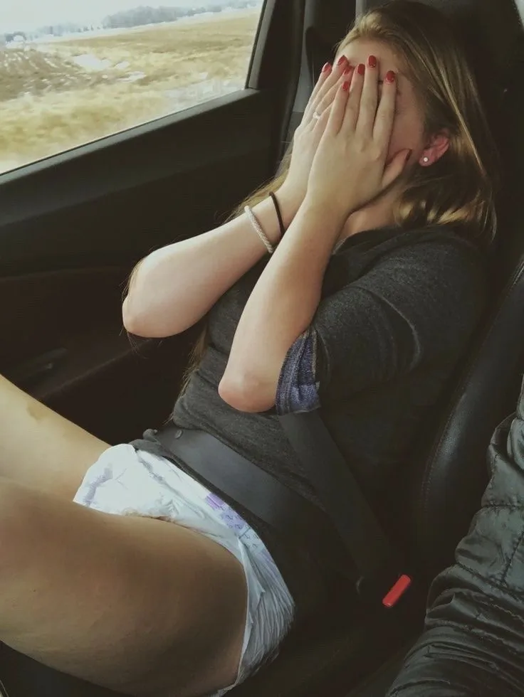 The ABDL girl covers her face in the car, embarrassed, wearing only a diaper on her lower body.