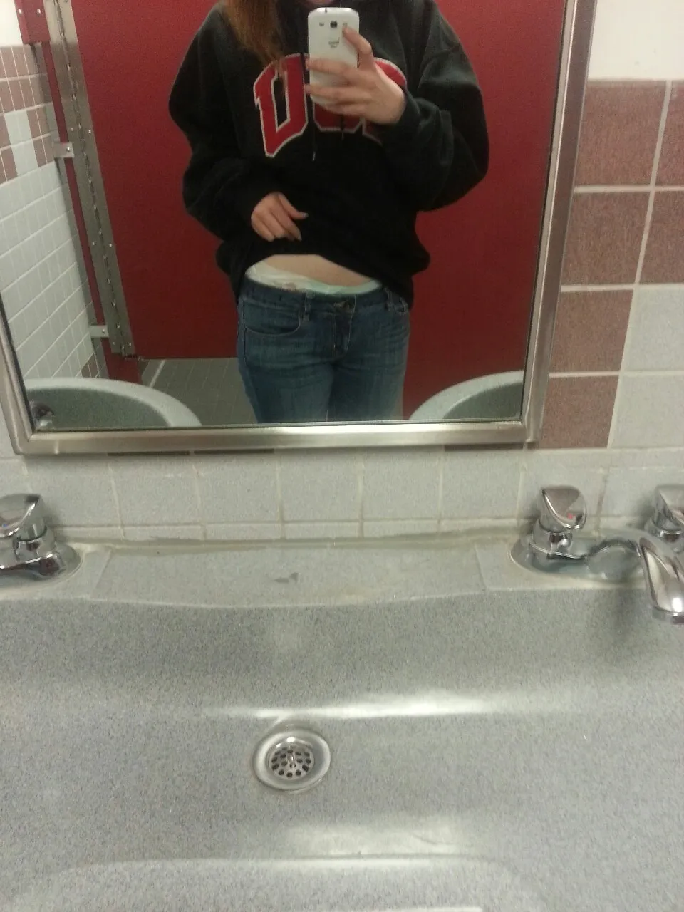 ABDL girl showing off the waistband of her diaper peeking out over her jeans in the bathroom.