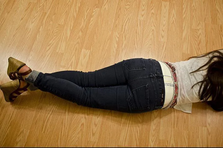 An ABDL girl is lying face down on the wooden floor, with the waistband of her diaper visible over her jeans.