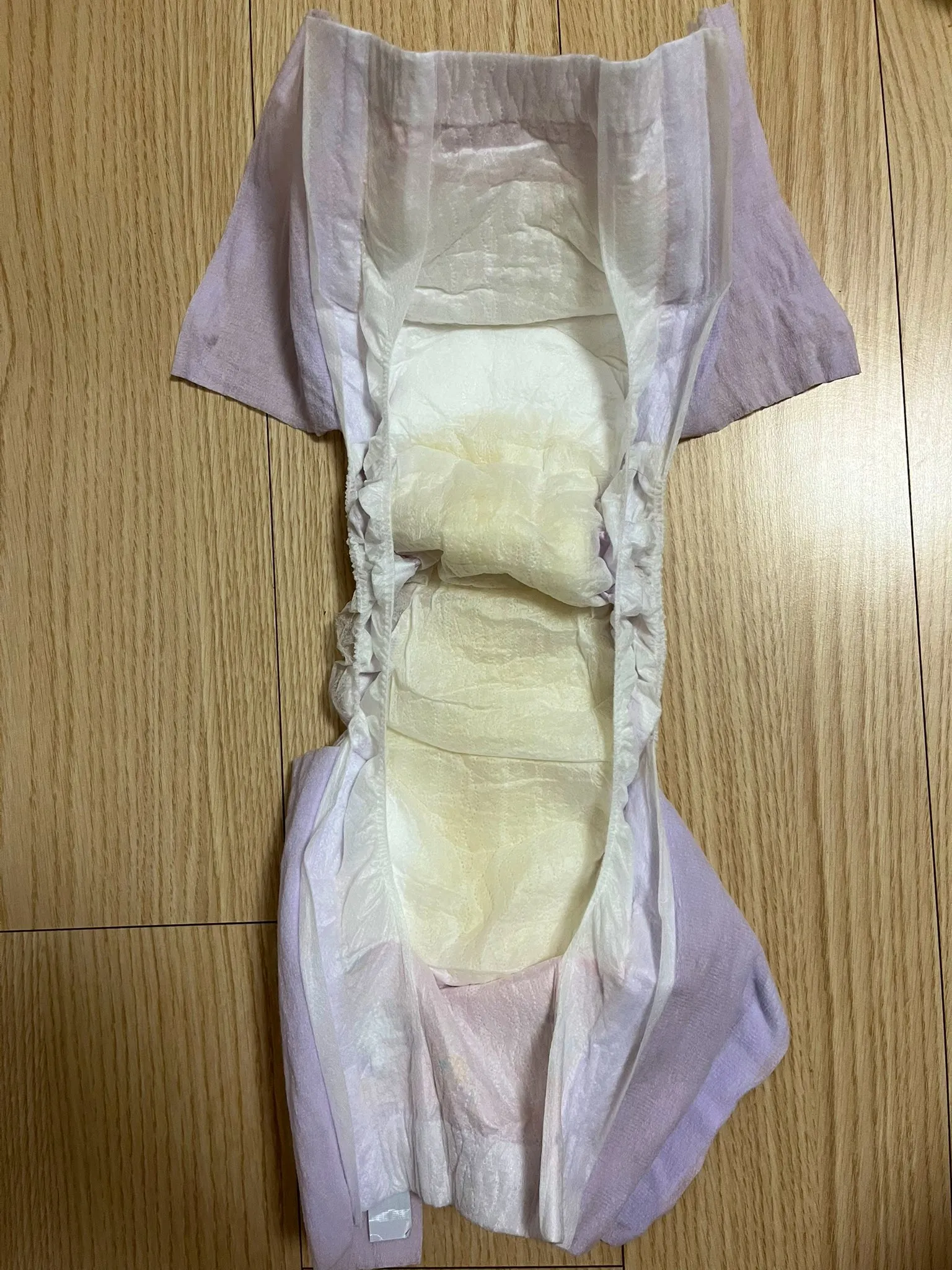 The ABDL girl unfolds the pull-up diaper filled with pee and places it on the floor.