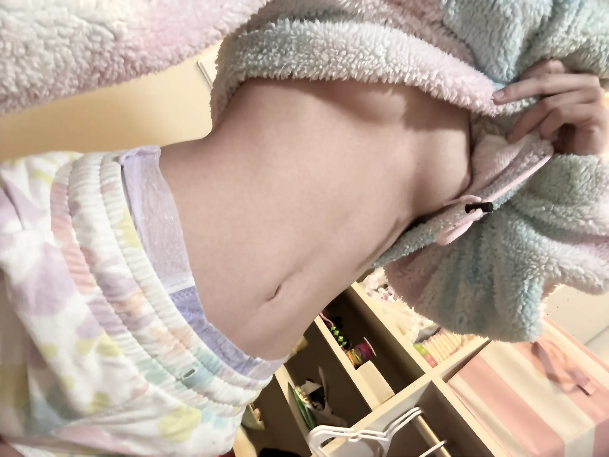The ABDL girl lifts her fleece top to show off her breasts and diaper waistband.