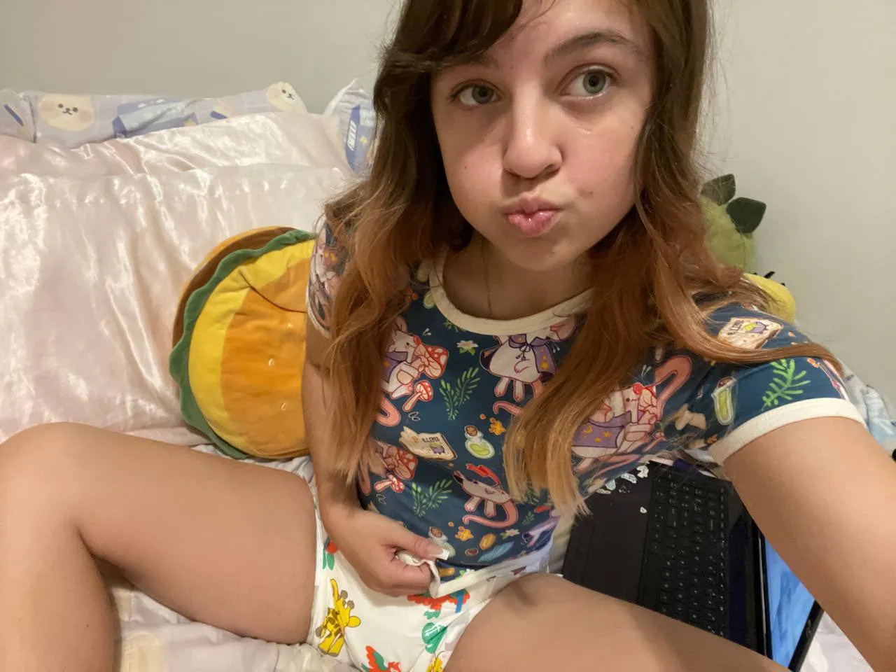 ABDL girl sits on the bed, opens her romper to show off her diaper.