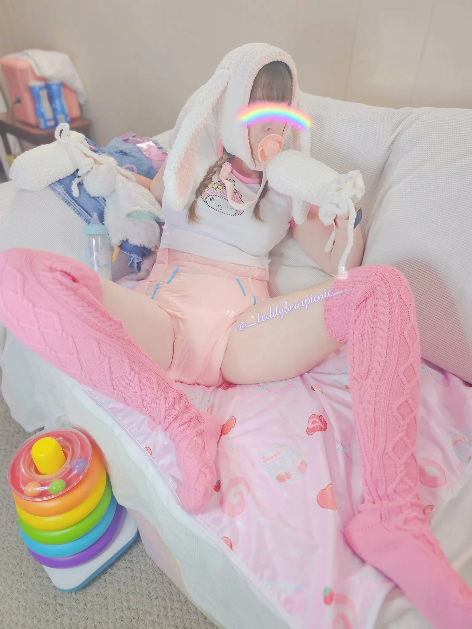 An ABDL girl wearing a bunny hat and pink knee-high socks spreads her legs to show off her diaper.