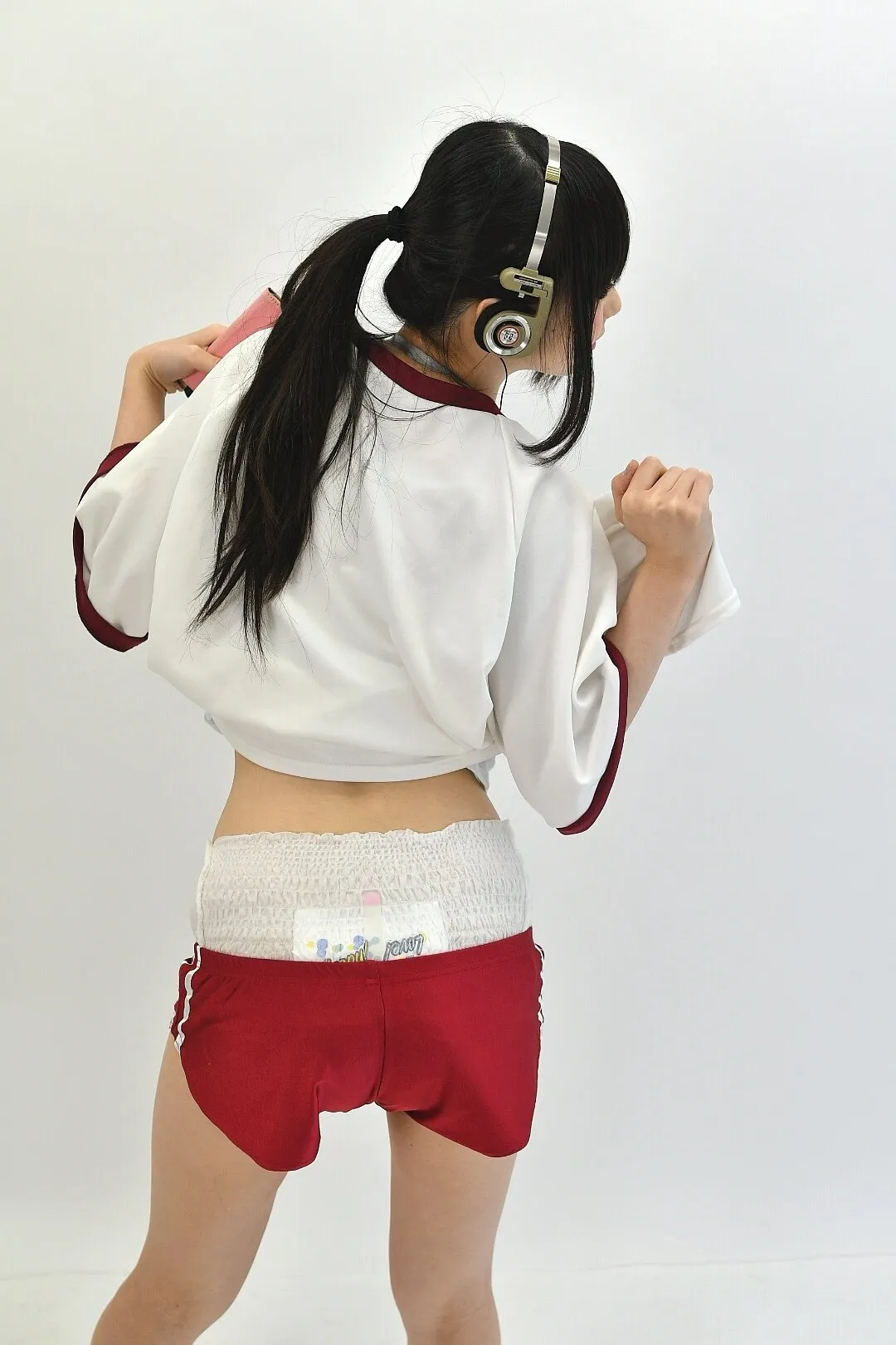 The ABDL girl lifts her top to reveal her wet diaper from behind.