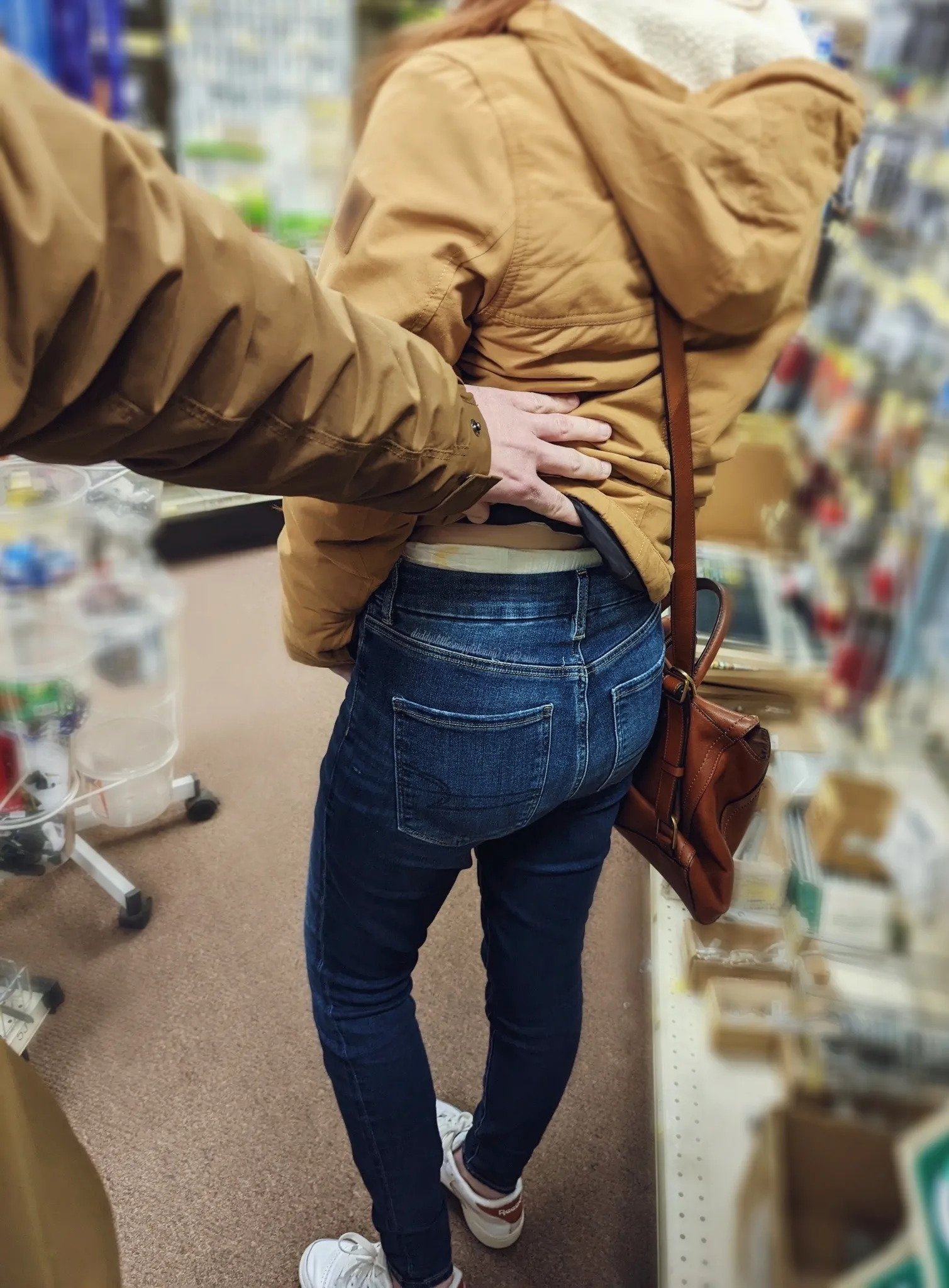 A woman wearing jeans in a store has her top lifted up by a man, revealing adult diapers.