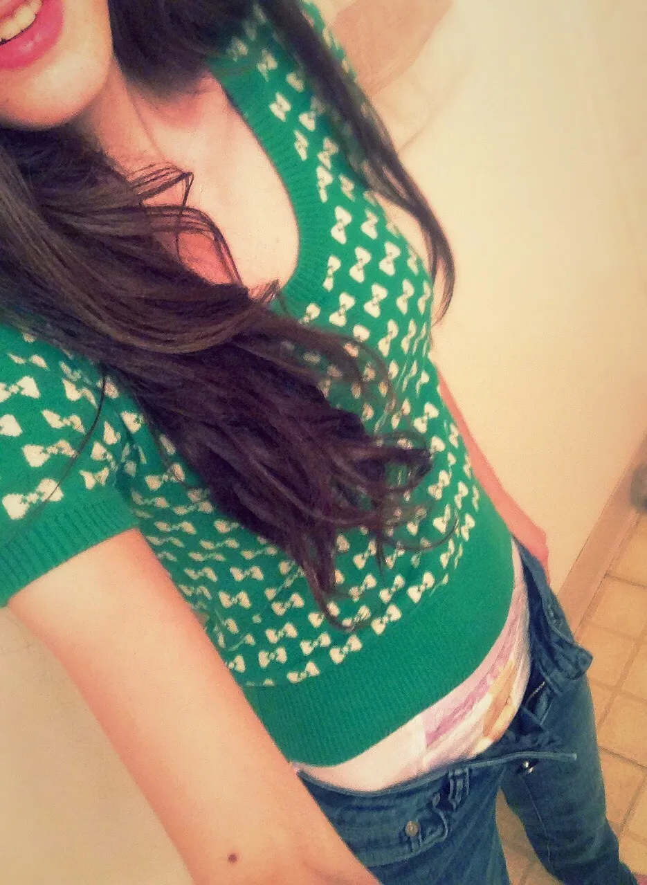 A girl wearing a green top with ribbon patterns pulls down her jeans, revealing a glimpse of her colorful patterned diaper.